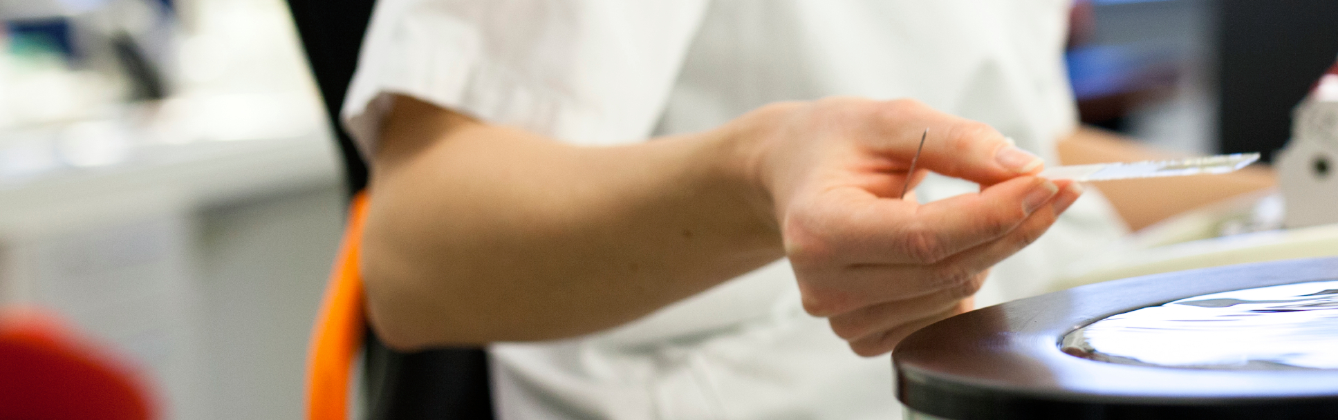 A person in a white lab coat working with a Leica RM machine, holding a thin glass plate in a laboratory