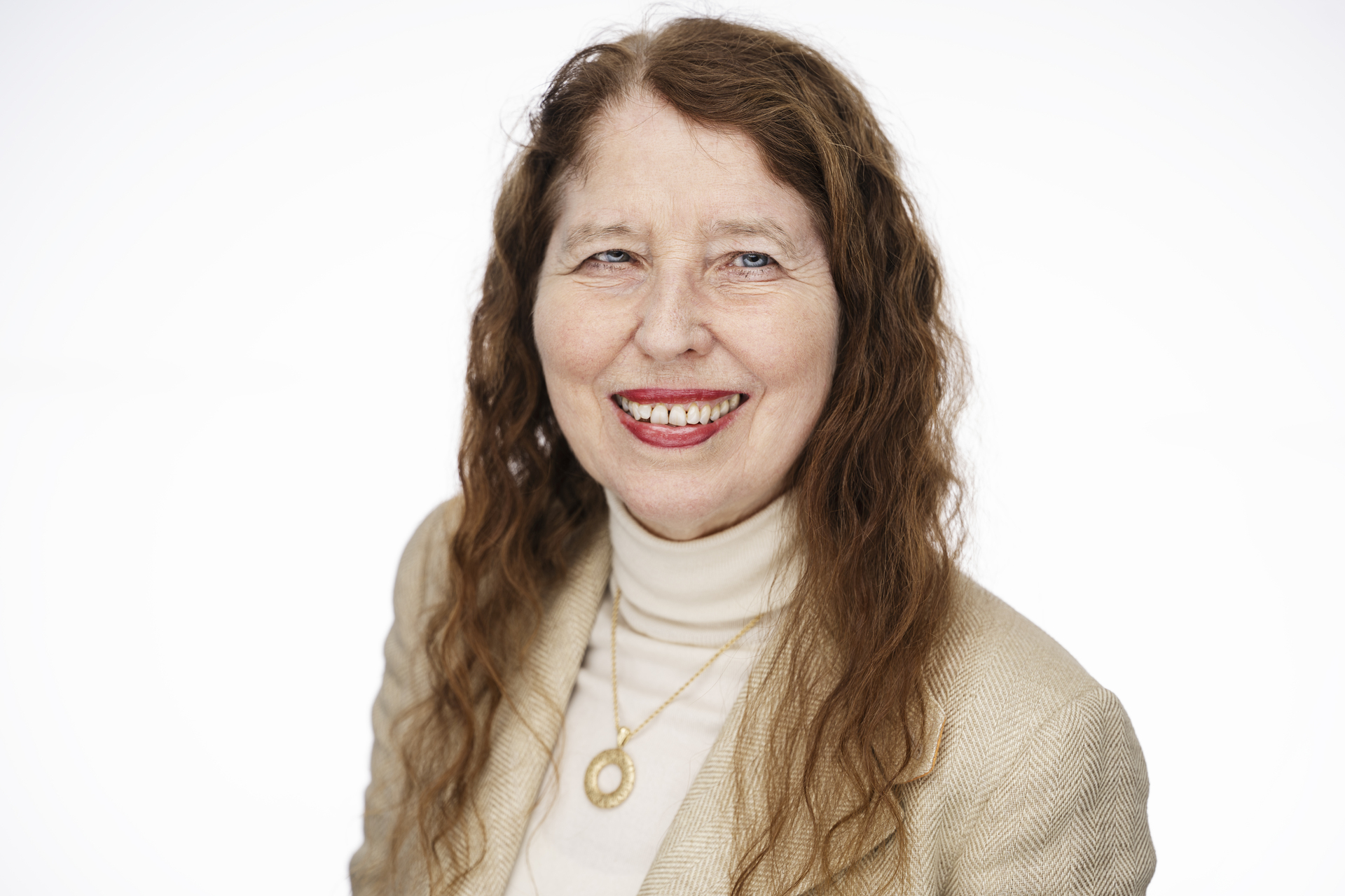 Lady with long red hair, sweater with a high neck and suit jacket. Looking straight into the camera. Wallpaper white