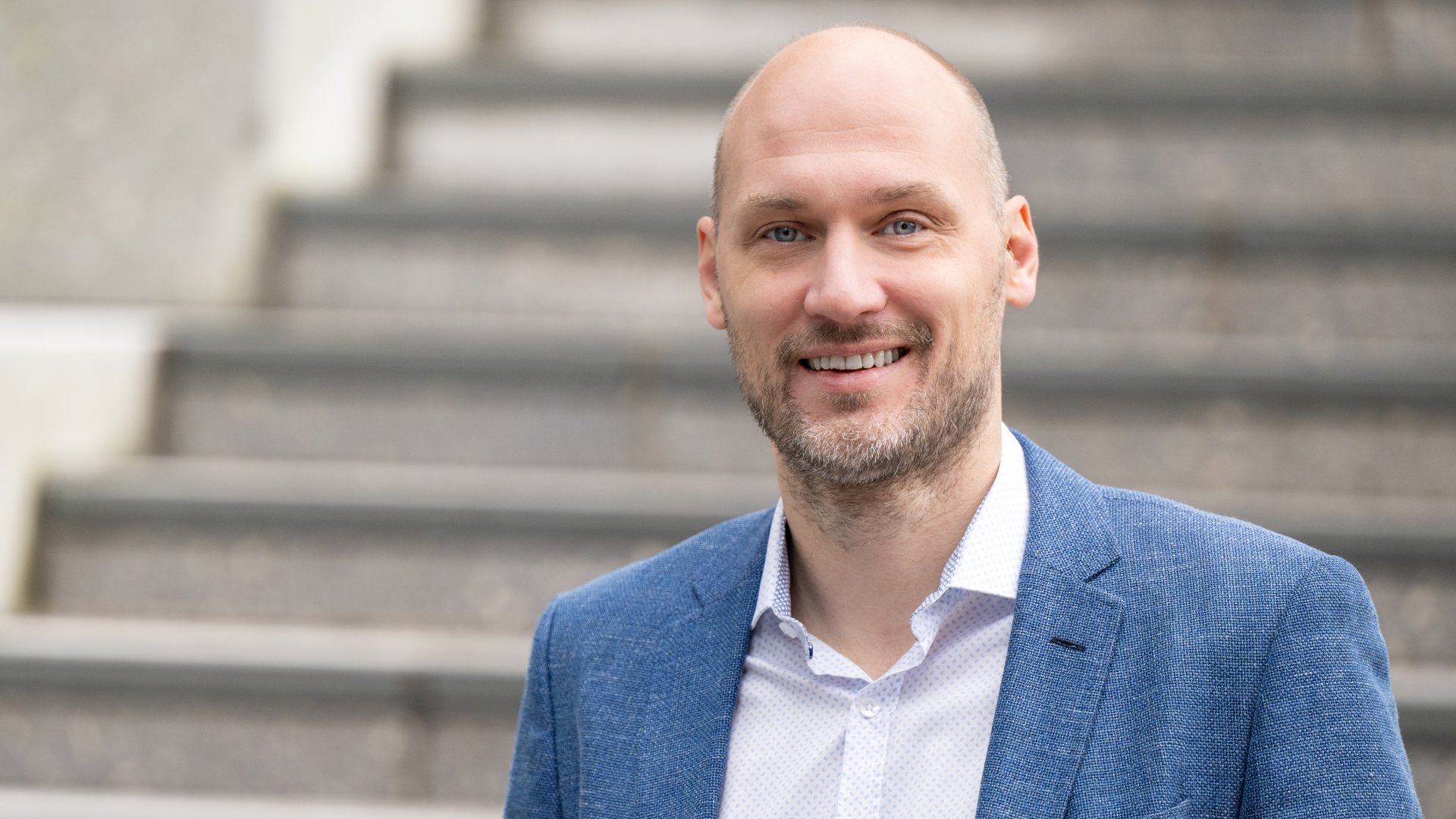 Mann med prikkete hvit skjorte og bl&aring; blazer som ser inn i kamera