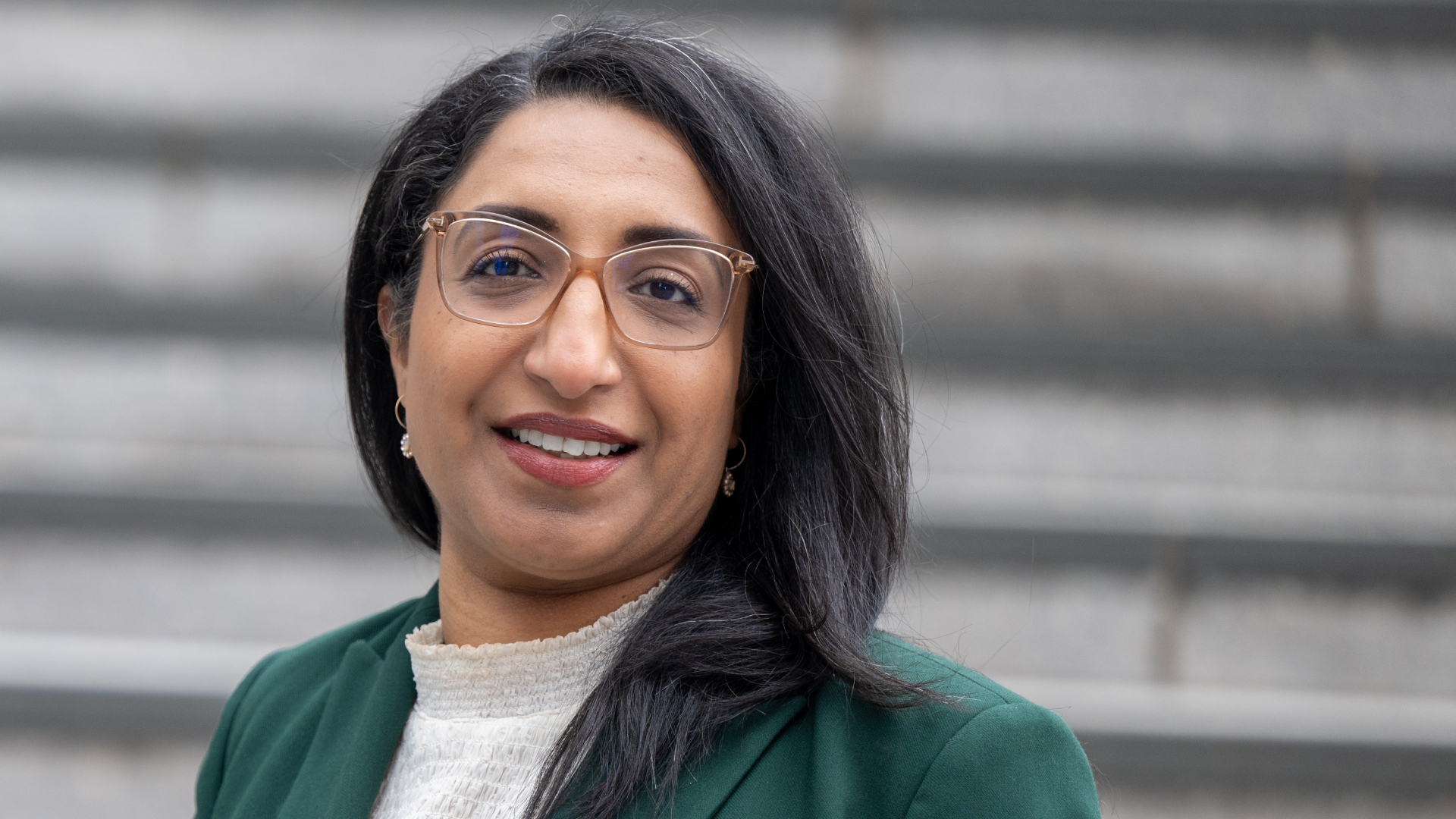 Kvinne med briller og m&oslash;rkt h&aring;r, ikledd gr&oslash;nn jakke som ser inn i kamera