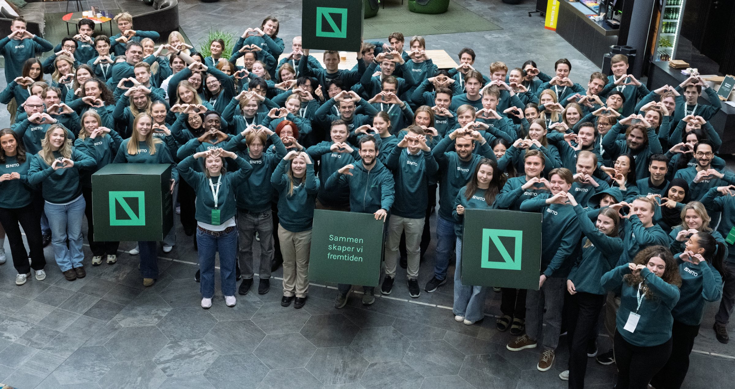 En stor gruppe unge i grønne NITO-gensere former hjerter med hendene.