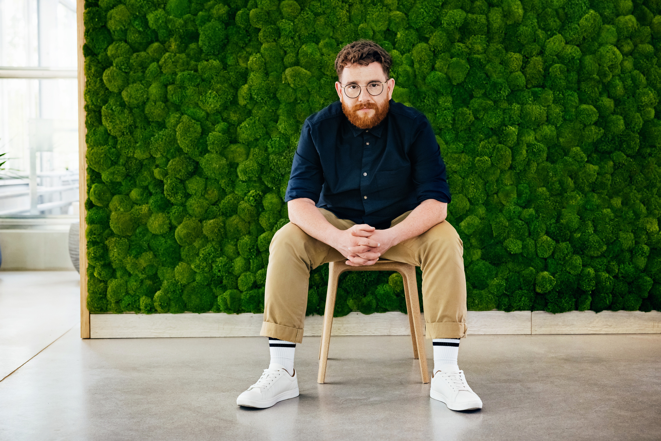 En mann som sitter på en krakk med grønn bakgrunn bestående av trær.