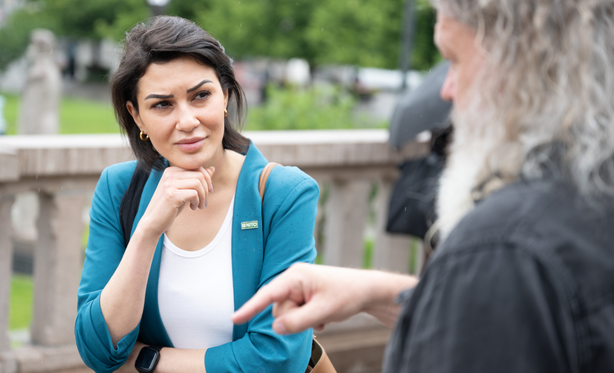 Kvinne i turkis blazer og m&oslash;rkt h&aring;r, og en mann med langt gr&aring;tt h&aring;r