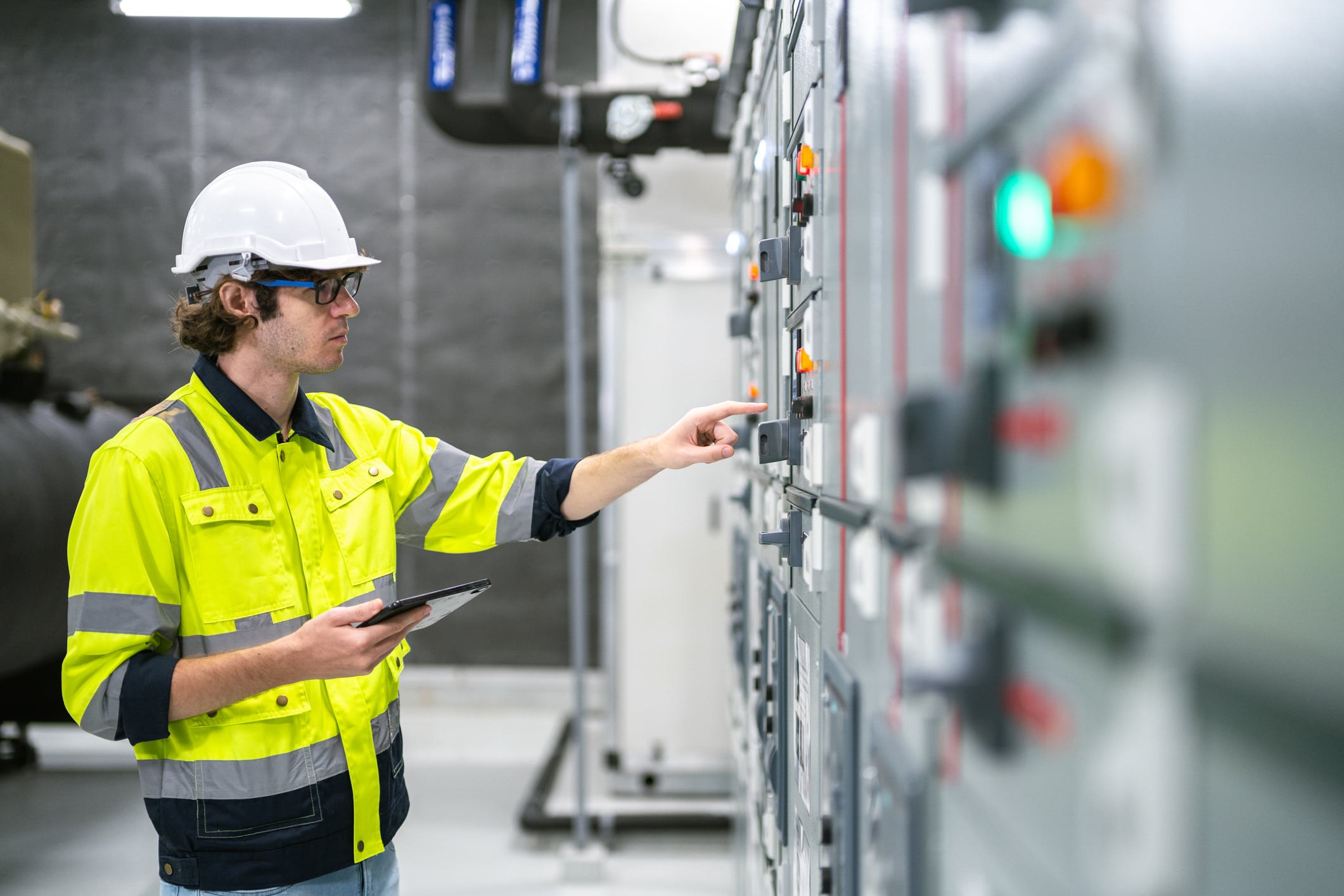 One person inspects and operates an industrial electrical control panel in a technical environment