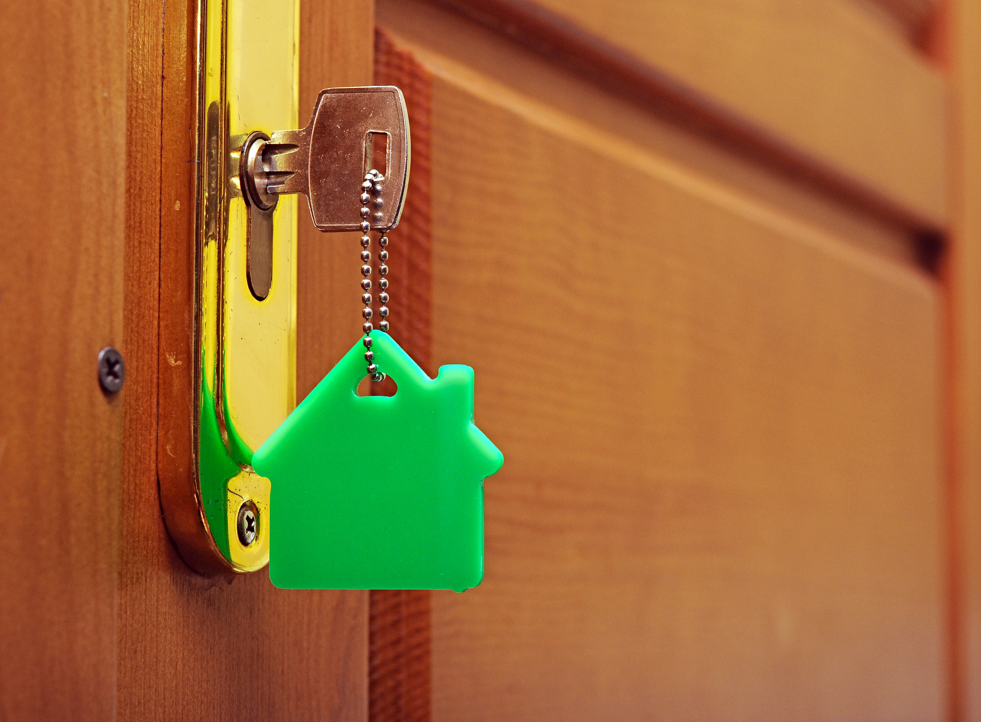 Et nøkkel i et nøkkelhull. Nøkken har en nøkkelring som er et grønt hus.