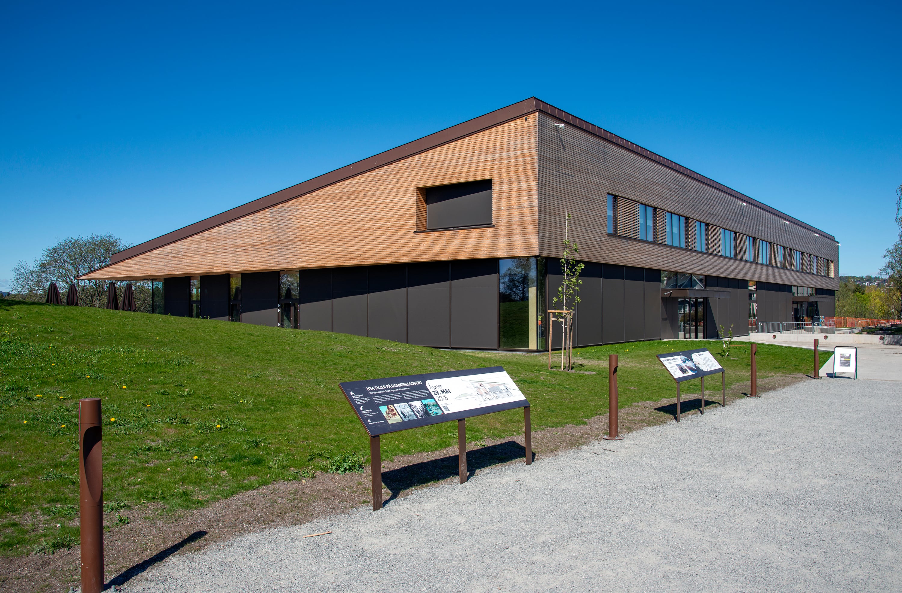 Picture of the new regional history centre at Domkirkeodden with signs in the foreground. Low wooden house with windows. The picture was taken against a corner of the house. Credit: Geir Ove Andreassen, Anno Domkirkeodden history center