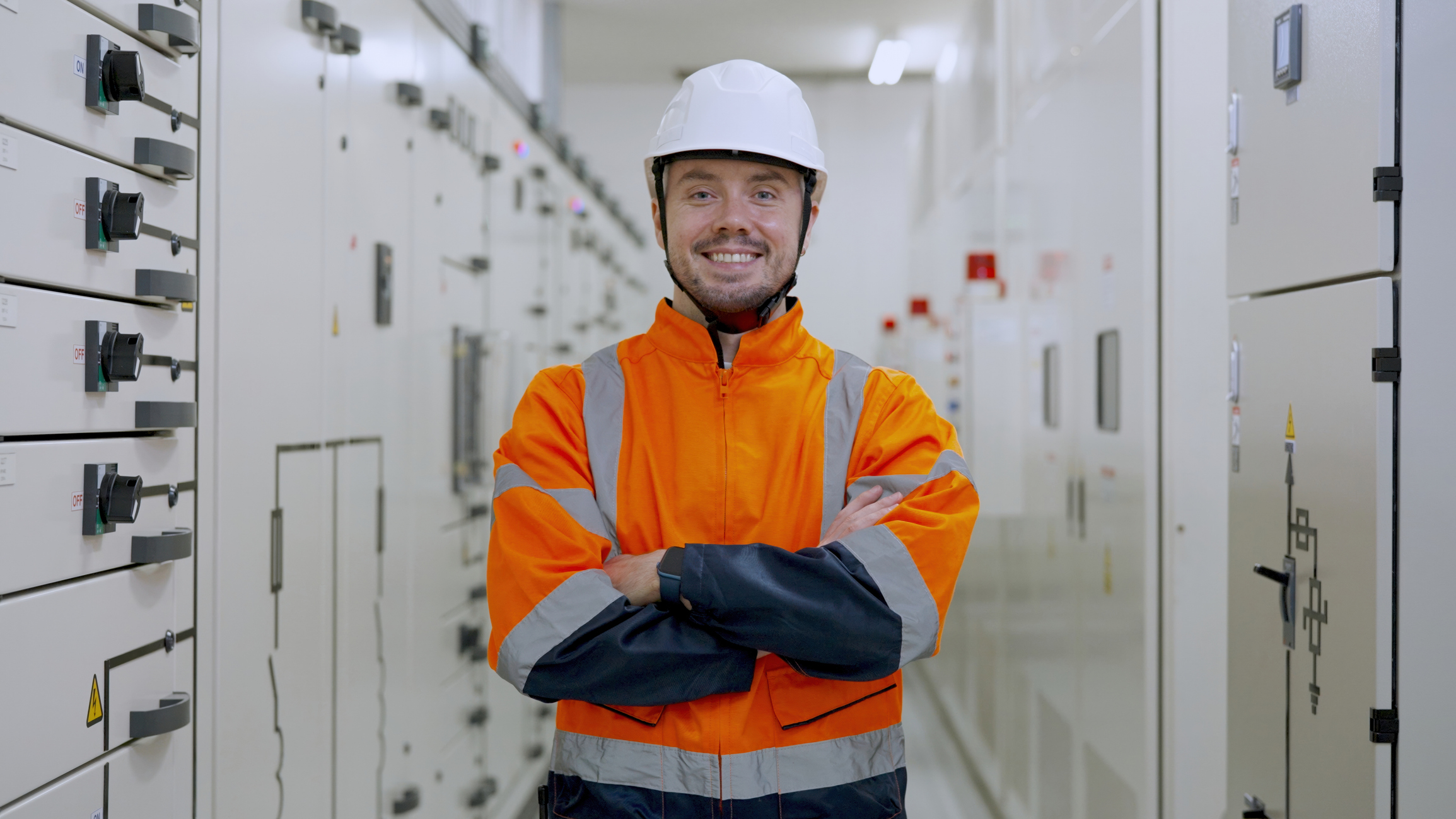 Elektroingeniør står smilende foran elektriske systemer