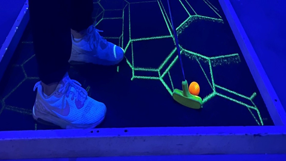 Nærbilde av person som spiller minigolf innendørs. Neonfarger 