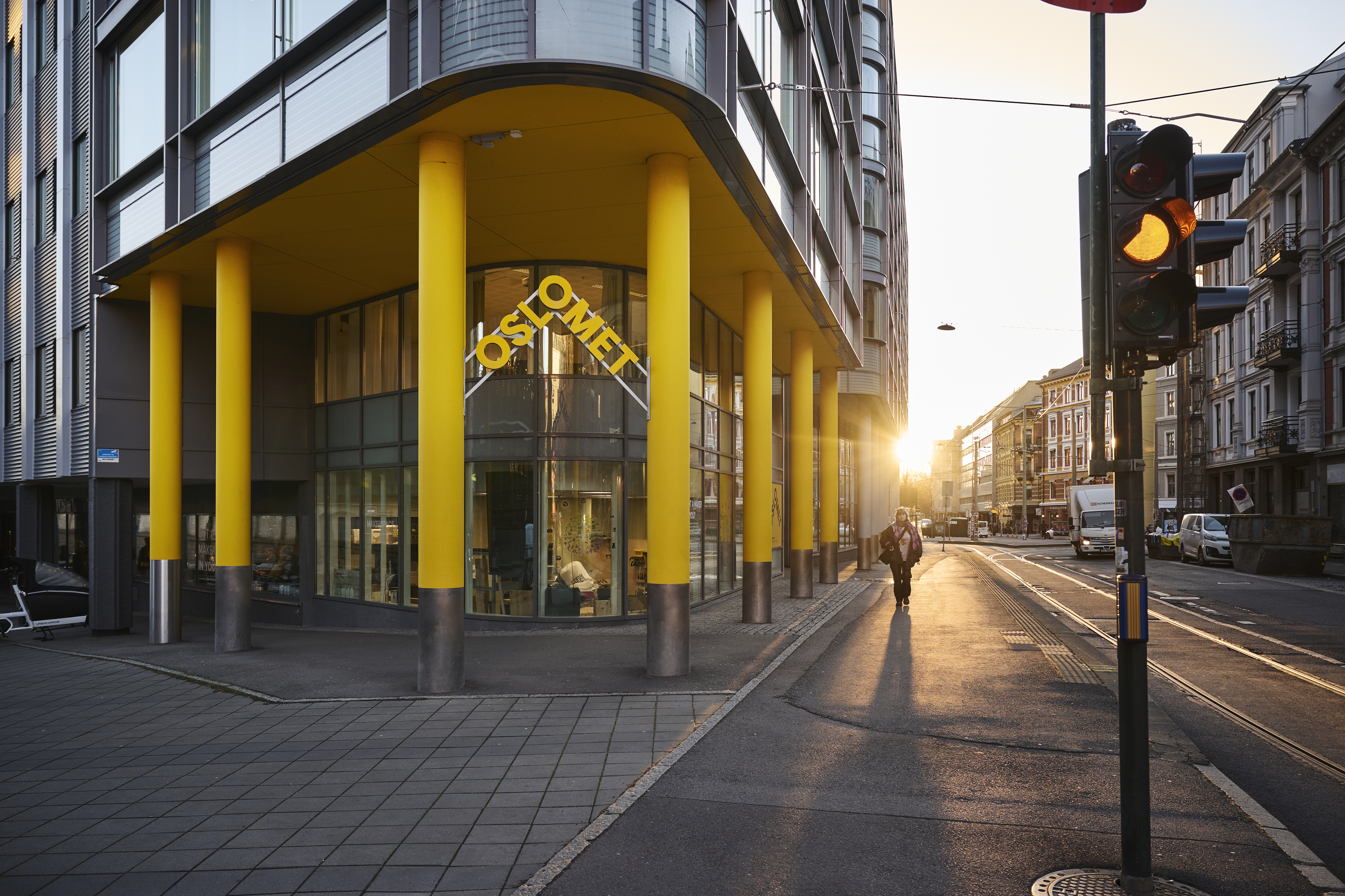 Bygård med gule søyler på hjørnet, store vinduer og gatebilde i solnedgang med tomme gater og moderne arkitektur.