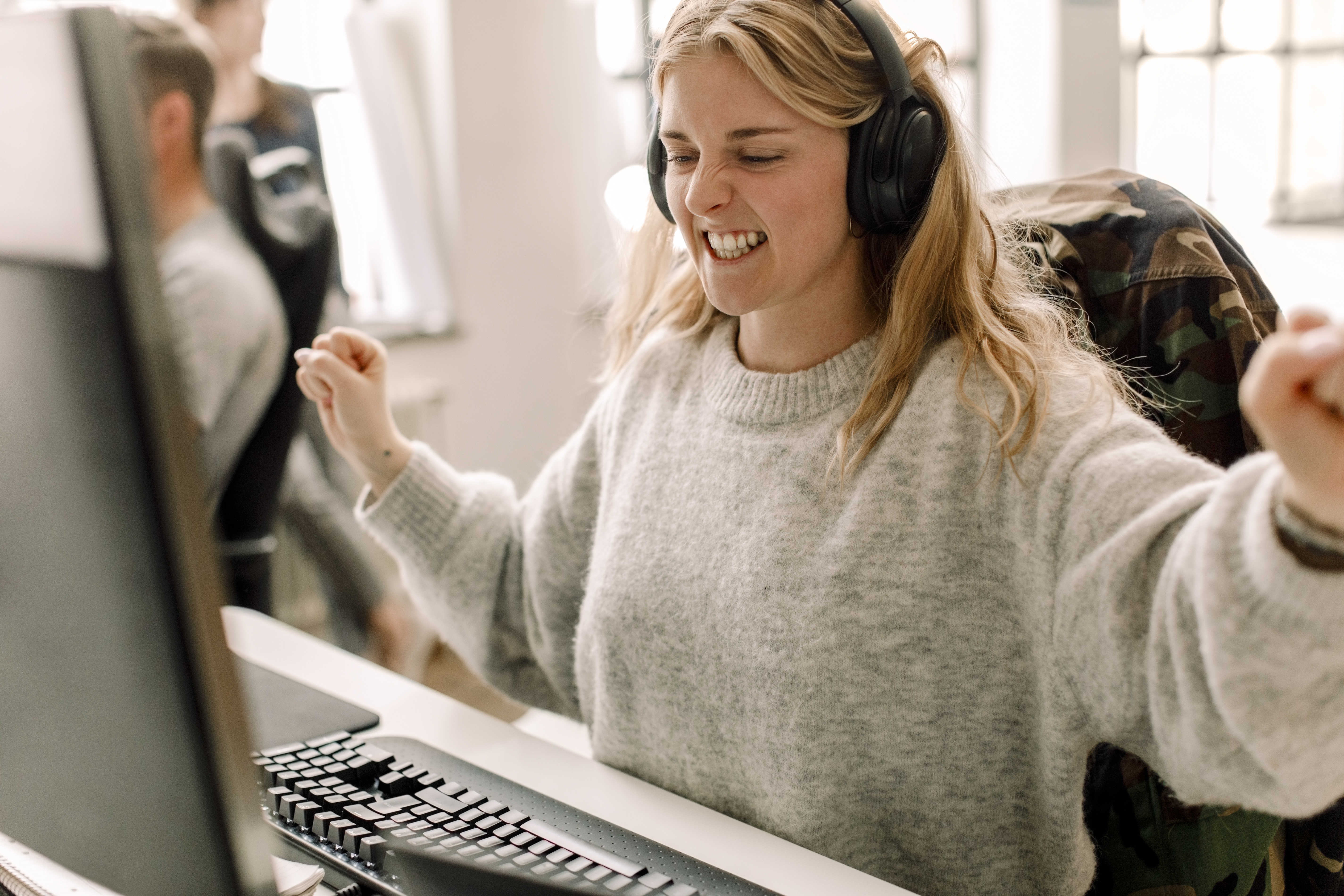 Ung blond kvinne med headset foran PC-skjerm, hun jubler