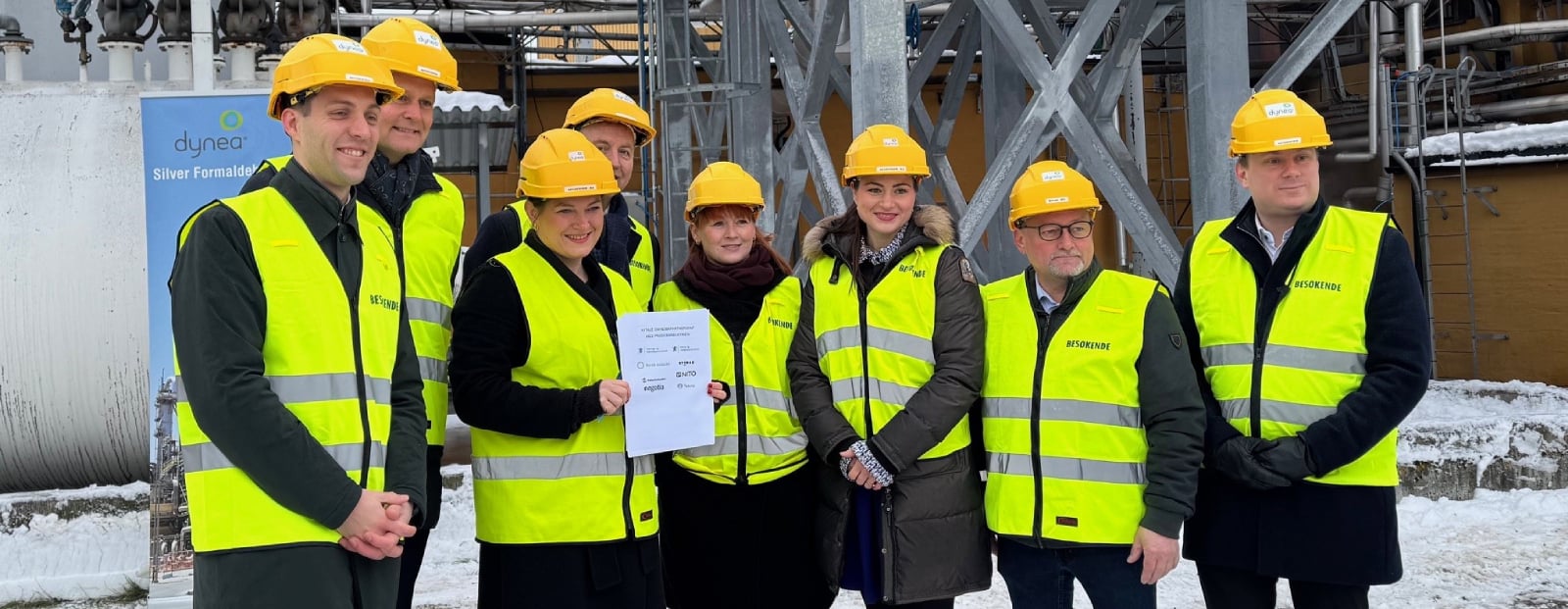 The photo shows eight people in helmets and reflective vests during an agreement signing with a focus on industry and sustainability.