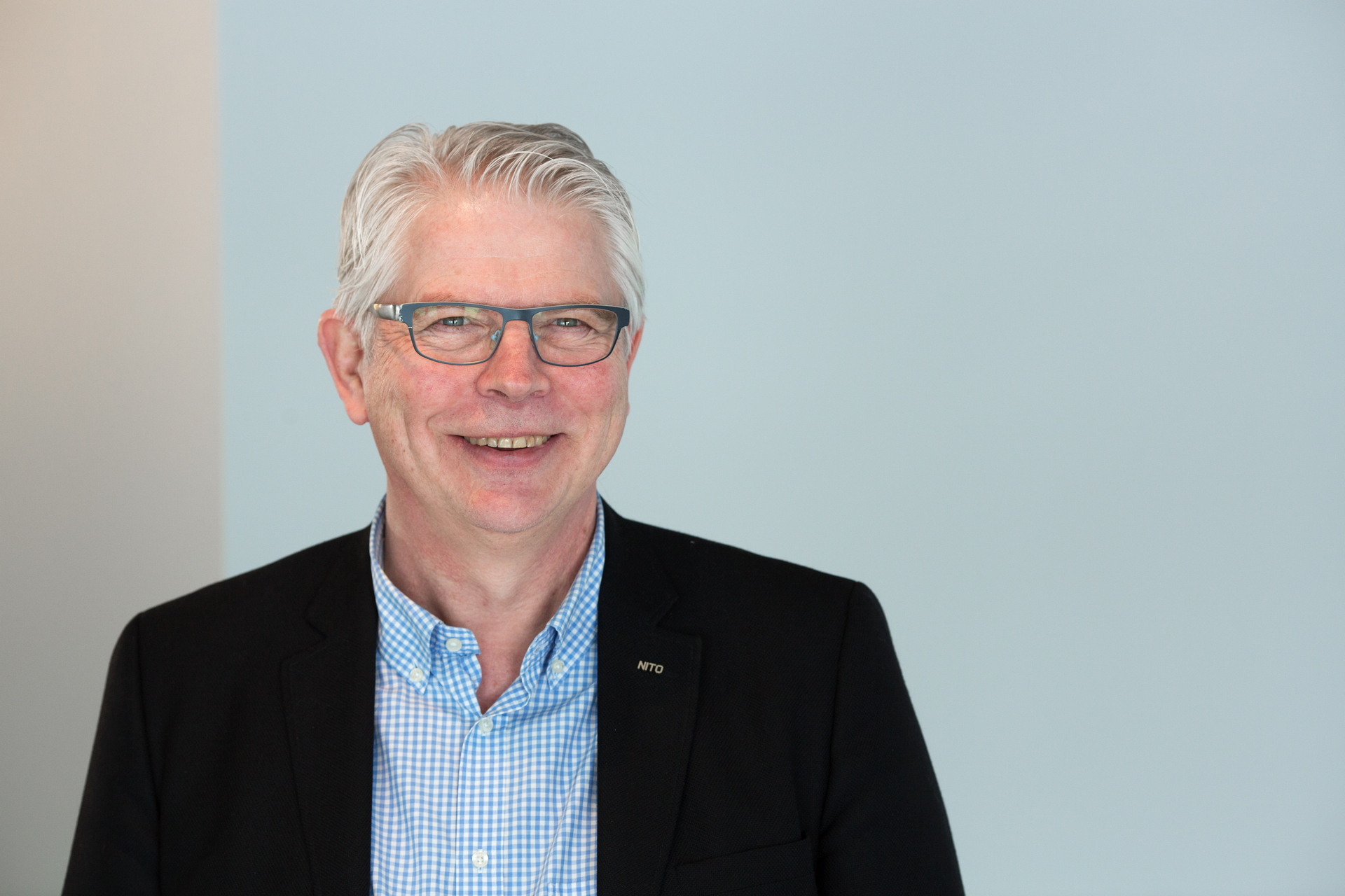 Mann med hvitt hår og briller har på seg blå skjorte og svart blazer