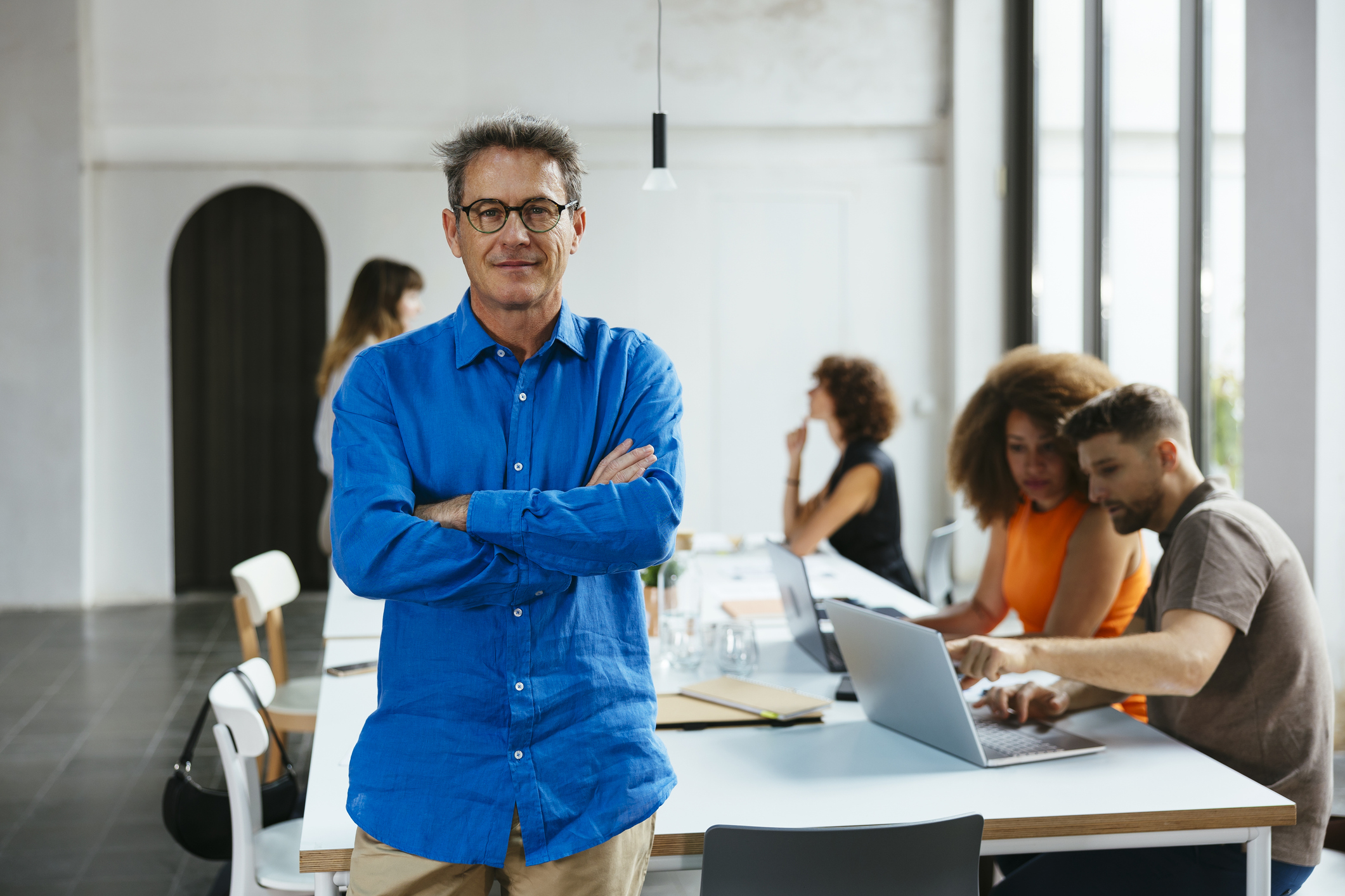 Mann i blå skjorte med armene i kors.