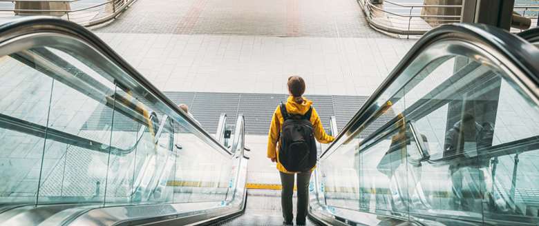 Ung, mannlig tillitsvalgt med ryggsekk på vei ned en rulletrapp for å delta på fagforeningskurs.