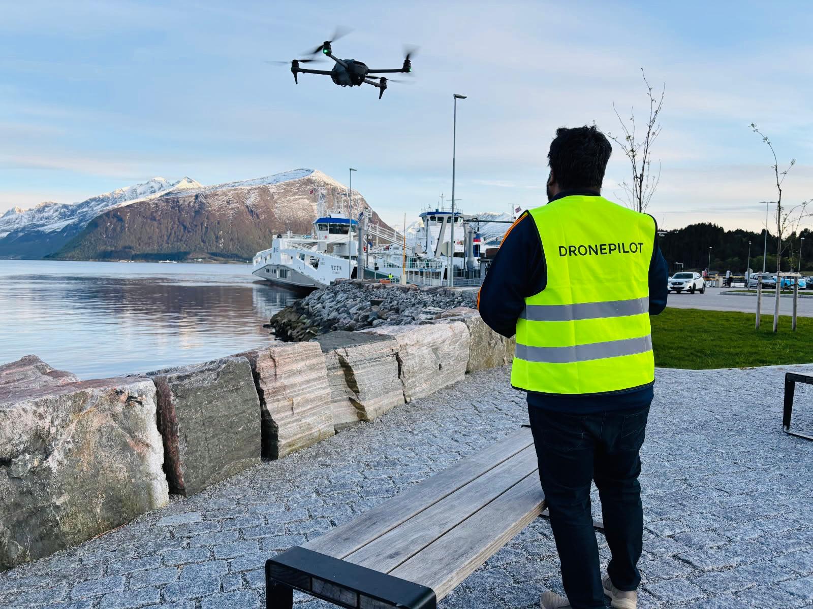 Dronen til dronepilot Rubwen har lettet fra bakken. Han står ved kanten av en fjord på Sunnmøre, klar for å ta video og bilder av båter som kjører forbi.
