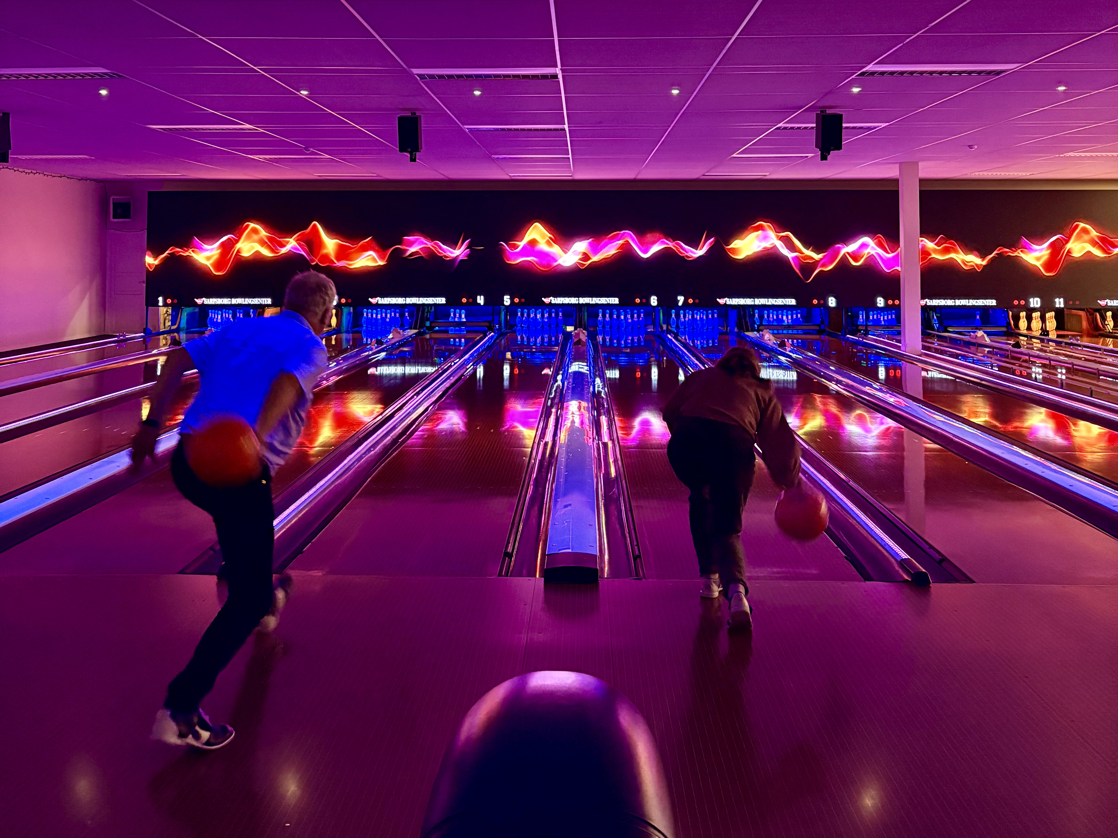 To personer som spiller bowling i et rom fylt med neonrosa lys