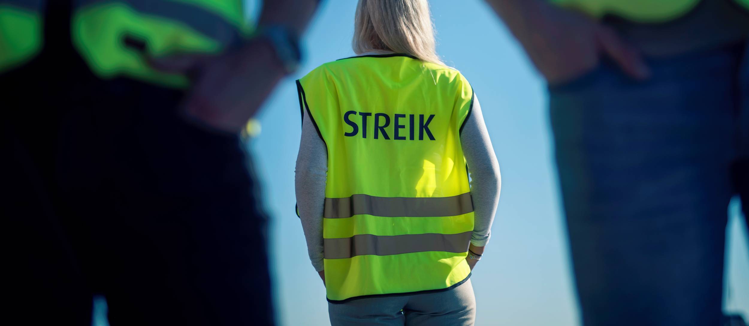 Person bakfra i gul refleksvest med ordet «STREIK» på ryggen.