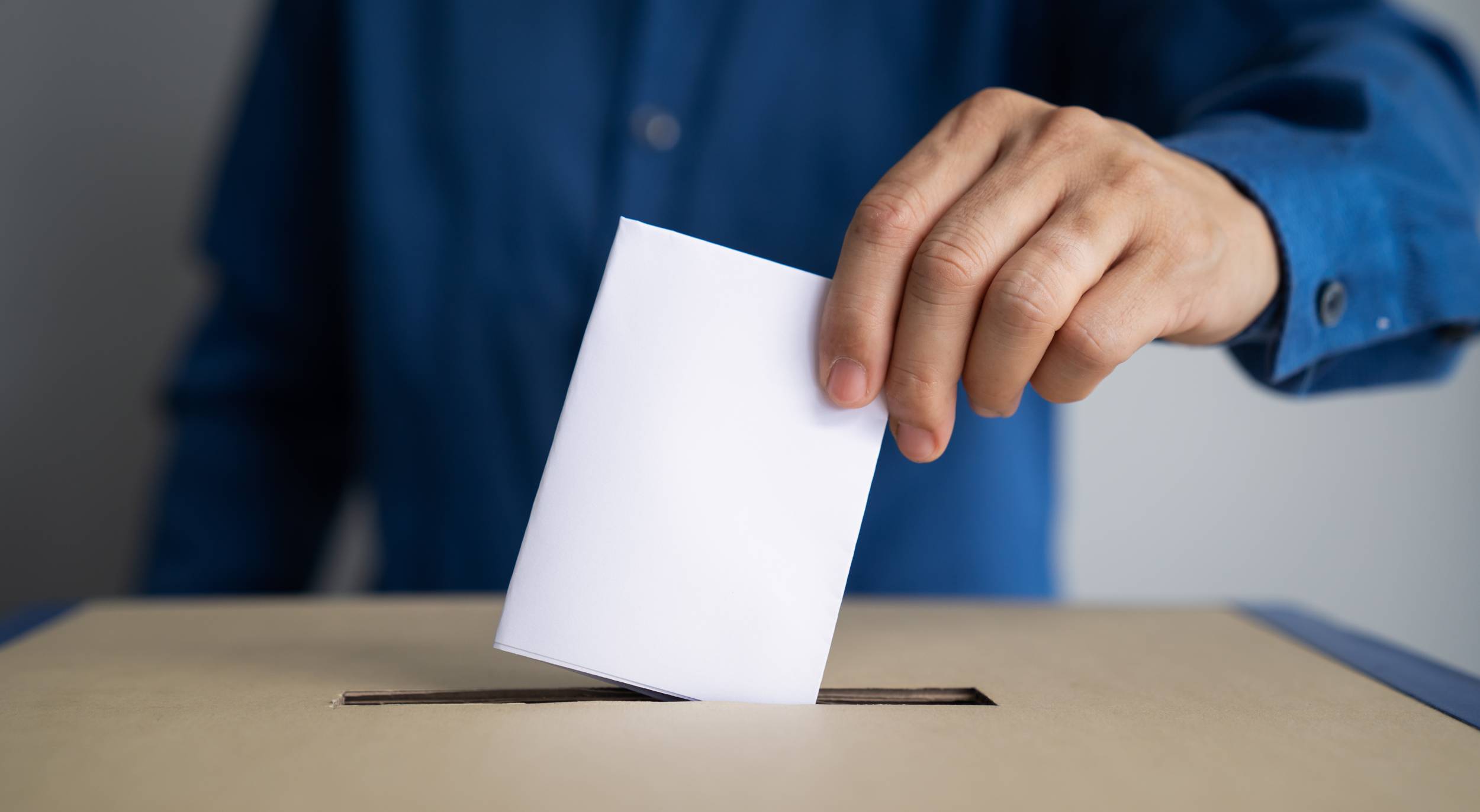 Illustrasjonsbilde av en mann i blå skjorte som putter en valgseddel ned i en stemmeurne