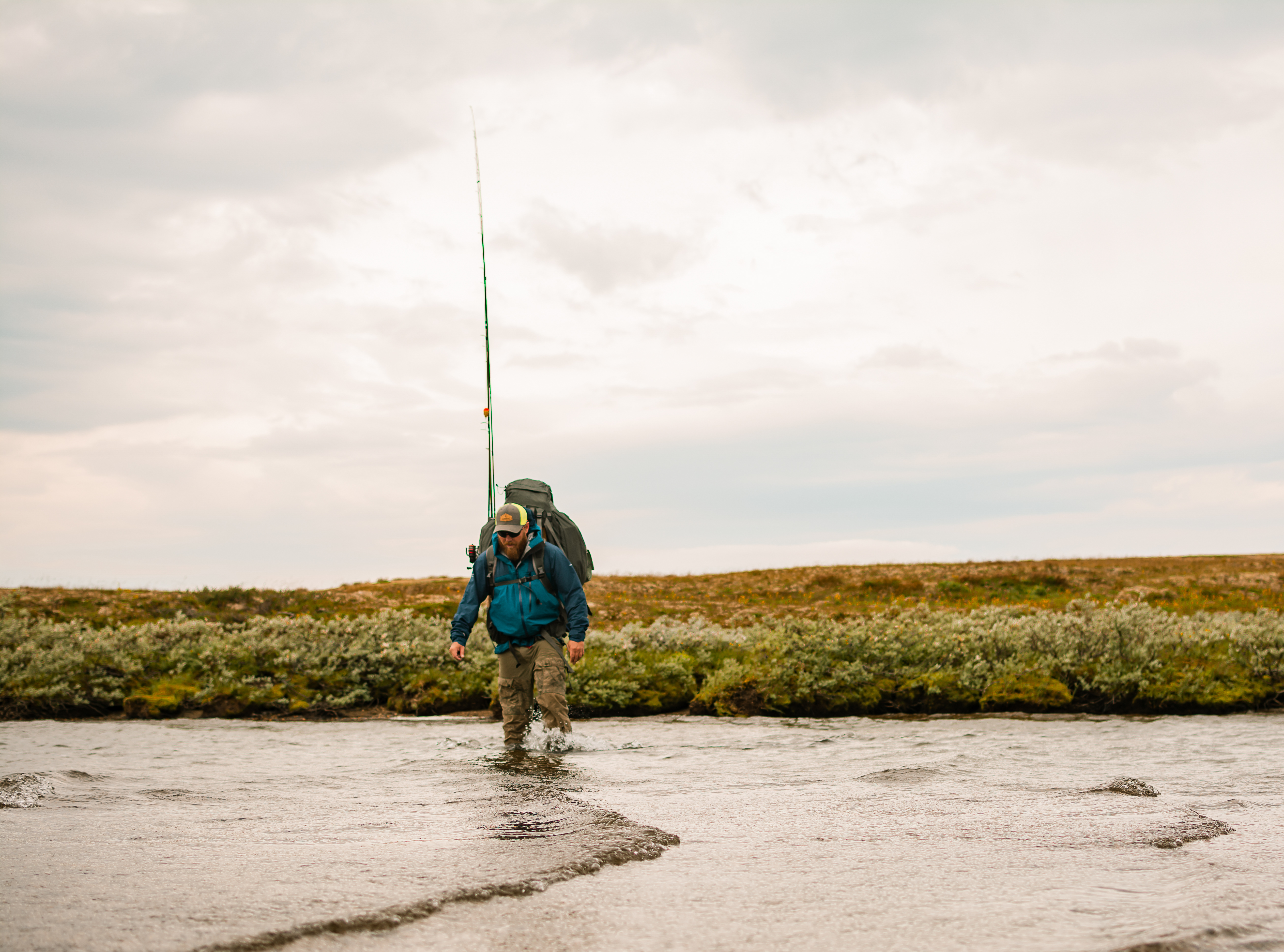 Mann med fiskeutstyr går over vannet på vidda. 