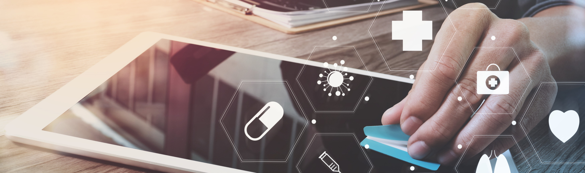 A hand uses a tablet, surrounded by digital health icons such as pill, heart and first aid – symbols of digital health technology.