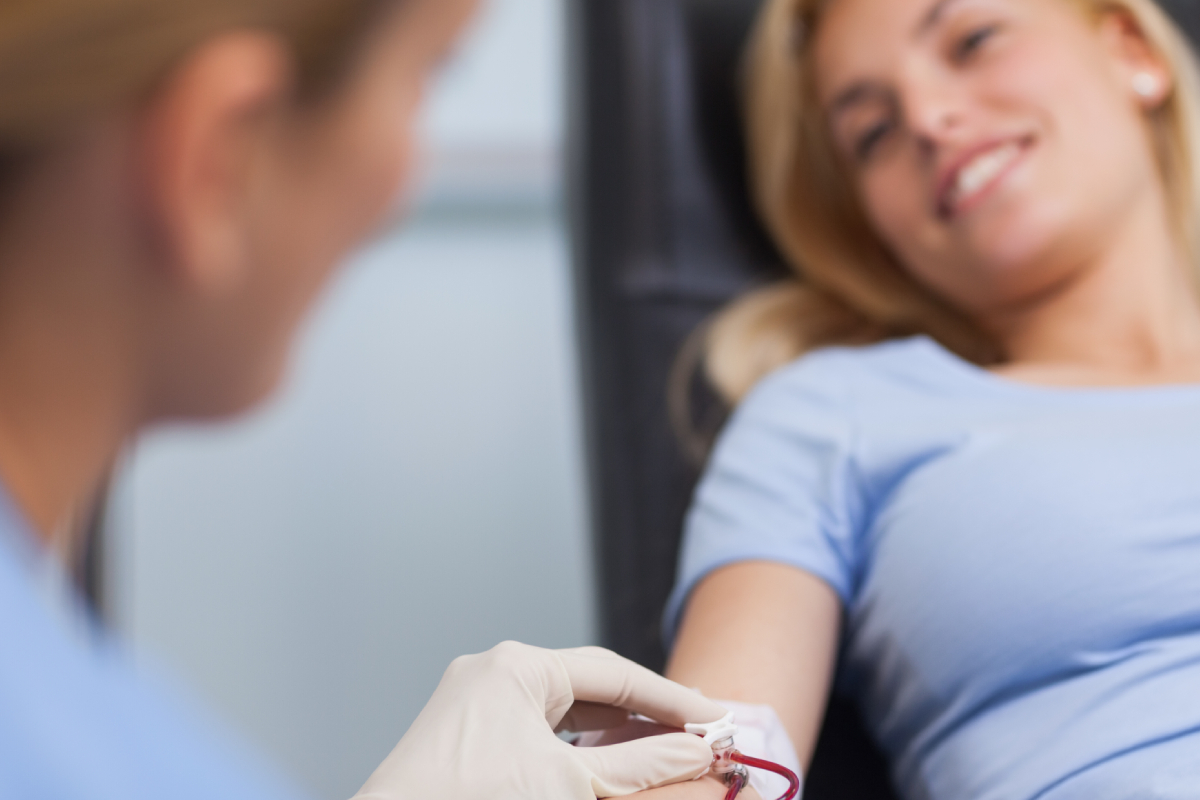 En person i lyseblått får tatt blodprøve av en annen med hansker, illustrerer en medisinsk prosess.