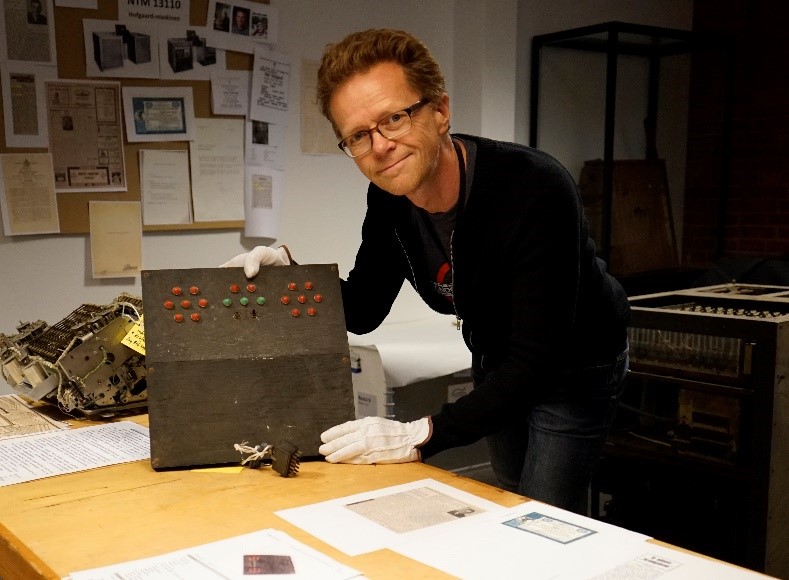 Ansatt på Teknisk museum holder opp en museumsgjenstand - Hofgaardmaskinen