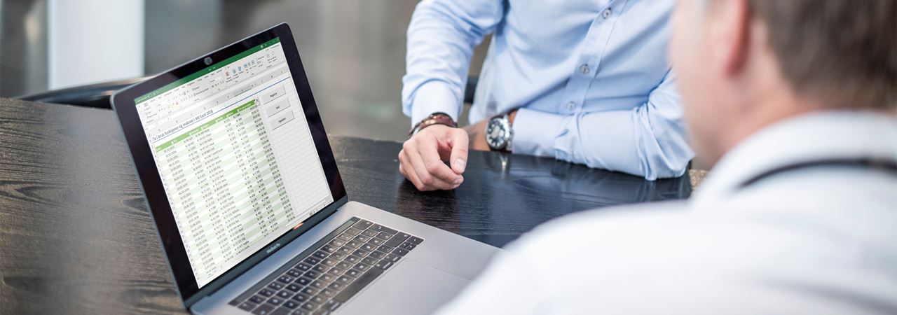 To personer som sitter foran en laptop med et excelark.
