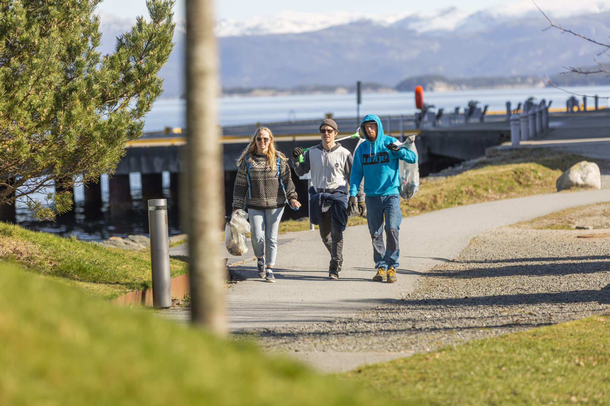 tre unge mennesker med friluftstøy, utendørs for å plukke søppel