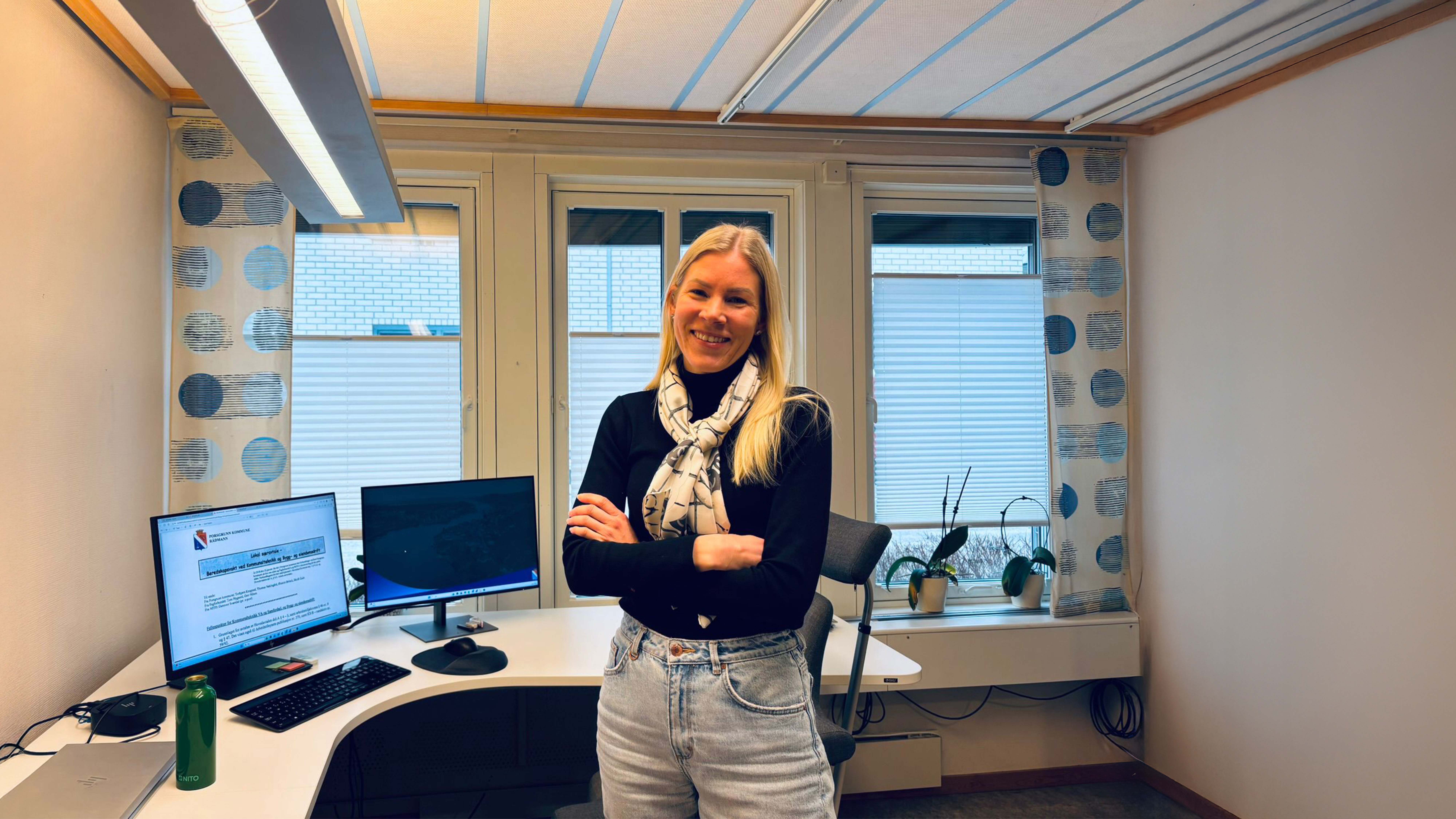 NITO union representative Kathrine Kværne standing in her office, in front of her computer. She has her arms crossed.